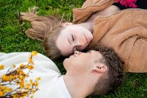 Casal jovem olhando um para o outro, enquanto descansando na grama com buquês de flores florescendo — Fotografia de Stock