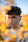Ritaglia viso maschile di copertura con rametti di fiori brillanti in fiore mentre guardi la fotocamera alla luce del giorno — Foto stock