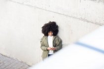 Hochwinkel der charismatischen jungen afroamerikanischen Millennials mit lockigem Haar, die lachen und wegschauen, während sie an sonnigen Tagen ihr Smartphone im Park benutzen — Stockfoto