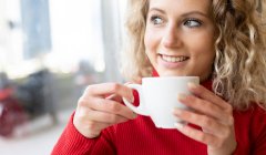 Donna sognante seduta a tavola nel caffè e che beve bevande calde mentre si gode il fine settimana e guarda fuori dalla finestra — Foto stock