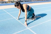 Side view of sportswoman standing in starting blocks in crouch start position during training at stadium in summer — Stock Photo