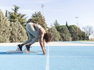 Side view of African American female runner in starting blocks standing in crouch position while getting ready for sprint at stadium during workout — Stock Photo