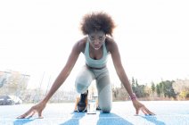 Von unten eine afroamerikanische Läuferin in den Startblöcken, die in geduckter Position steht, während sie sich im Stadion auf den Sprint vorbereitet — Stockfoto