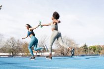 Adaptez-vous aux athlètes féminines multiraciales passant le bâton tout en courant le long de la piste au stade pendant la course de relais — Photo de stock