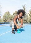 Сосредоточенная черная спортсменка делает упражнения с гантелями во время тренировок на стадионе летом и с нетерпением ждет — стоковое фото