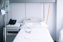 Leeres Bett mit Schwesternruftaste in der Nähe von IV stehen in hell ausgestatteter Station in zeitgenössischem Krankenhaus — Stockfoto