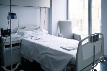 Порожнє ліжко з кнопкою виклику медсестри біля IV стенду у світло обладнаному приміщенні в сучасній лікарні — стокове фото