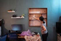 Seitenansicht der ethnischen Frau mit Pinsel Malerei Holzregale in weißer Farbe bei der Renovierung von Möbeln — Stockfoto