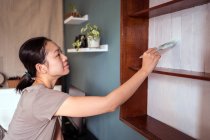 Side view of ethnic female with paintbrush painting wooden shelves in white color while renovating furniture — Stock Photo