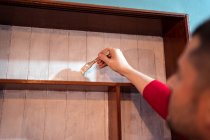 Vista laterale maschio con pennello pittura mensole in legno di colore bianco durante la ristrutturazione di mobili — Foto stock