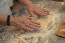 De cima de cultura cozinheiro idoso irreconhecível rolando crosta na mesa com farinha enquanto cozinha na cozinha em casa — Fotografia de Stock