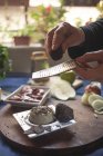 Cultive o chef irreconhecível polvilhando queijo macio com trufa usando ralador enquanto cozinha na mesa em casa — Fotografia de Stock