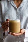 Colheita fêmea irreconhecível de pé com copo de vidro de café caseiro com leite para o café da manhã — Fotografia de Stock