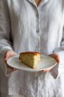 Ernte anonyme Frau steht mit Stück hausgemachten Biskuitkuchen auf Teller zum Frühstück zubereitet — Stockfoto
