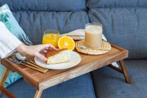 Hohe Winkel der Ernte gesichtslose Frau nimmt Stück hausgemachten Biskuitkuchen von Tablett mit Tasse Kaffee und Glas Orangensaft während des Frühstücks zu Hause — Stockfoto