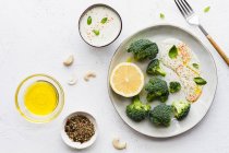Top view of tasty broccoli with fresh lemon and sauce near bowls with olive oil and spice mix on table — Stock Photo