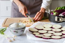 Анонімний шеф-кухар подрібнює зелену цибулю, роблячи закуску з баклажанами та сиром на кухні — стокове фото