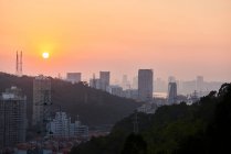 Vue paisible de la métropole contemporaine avec des gratte-ciel et des bâtiments résidentiels sous le ciel orange au crépuscule — Photo de stock