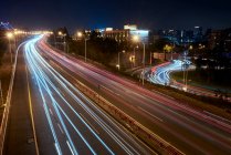 Lange belichtete Asphaltstraße mit fahrenden Fahrzeugen in zeitgenössischer Großstadt in der Nacht — Stockfoto