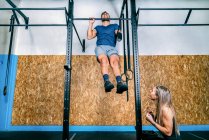 Young female athlete training and helping handicapped sportsman on horizontal bar during training in gym — Stock Photo