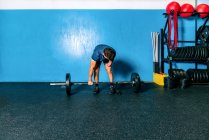 Poderoso atleta masculino sem mão levantando peso pesado durante o treinamento funcional perto de equipamentos esportivos no ginásio — Fotografia de Stock