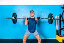 Atleta masculino poderoso sem gritos de mão enquanto levanta peso pesado durante o treinamento funcional perto de equipamentos esportivos no ginásio — Fotografia de Stock