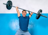 Potente atleta masculino sin gritos de mano mientras levanta peso pesado durante el entrenamiento funcional cerca de equipos deportivos en el gimnasio - foto de stock