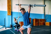Desportista poderoso com atleta masculino deficiente levantando pesos pesados e olhando para a frente durante o treinamento funcional em ginásio — Fotografia de Stock
