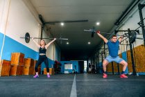 From below powerful sportswoman with handicapped male athlete lifting heavy weights and looking forward during functional training in gymnasium — Stock Photo