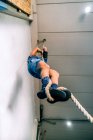 From below unrecognizable disabled male athlete in sports clothes climbing workout rope near bright wall in gym — Stock Photo