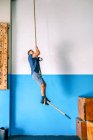 Vista lateral do atleta masculino com deficiência em roupas esportivas trepar corda de treino perto de parede brilhante no ginásio — Fotografia de Stock