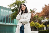 Bajo ángulo de la mujer empresaria alegre hablando en el teléfono inteligente y de pie en la calle mientras discute el proyecto de negocios y mirando hacia otro lado - foto de stock