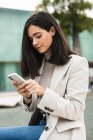 Vista laterale di imprenditrice concentrata che utilizza lo smartphone in strada mentre controlla i messaggi in e-mail — Foto stock
