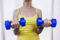 Crop anonymous fit female in yellow top doing arms exercise with dumbbells while working out in modern fitness center — Stock Photo