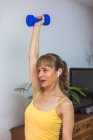 Sourire ajustement femelle en haut jaune faire des exercices de bras avec haltères tout en travaillant dans un centre de fitness moderne — Photo de stock