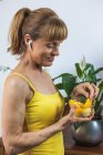 Crop side view glad adult female listening to music via earbuds and enjoying juicy fresh orange segment in glass bowl — Stock Photo