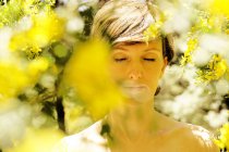 Ruhige erwachsene nackte Weibchen mit geschlossenen Augen ruhen im Garten in der Nähe blühenden Baum mit gelben Blüten an sonnigen Tag — Stockfoto