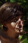 Verführerische junge nackte Frau mit dunklen Haaren sitzt in der Nähe von Farnbusch im üppigen tropischen Wald mit geschlossenen Augen an sonnigen Tagen — Stockfoto