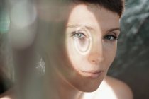Through glass of peaceful adult lady with short hair looking at camera on sunny day — Stock Photo