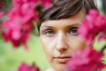 Crop feminino adulto pensativo com cabelo curto recriando no jardim verde perto de flores florescentes brilhantes e olhando para a câmera — Fotografia de Stock