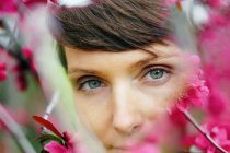 Кукурудза нахабна доросла жінка з коротким волоссям, що відпочиває в зеленому саду біля яскравих квітів і дивиться на камеру — стокове фото