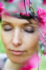 Cultivo pensativo adulto hembra con pelo corto recreando en jardín verde cerca de flores florecientes brillantes con los ojos cerrados - foto de stock