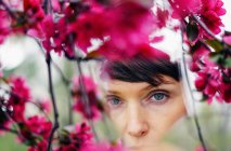 Задумчивый урожай взрослой женщины с короткими волосами воссоздания в зеленом саду рядом с яркими цветущими цветами и смотреть в камеру — стоковое фото