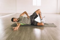 Повне тіло молодого орієнтованого спортсмена в активному одязі, що виконує High Side Plank з ногами піднімає вправи під час тренування в студії біля великого дзеркала стіни — стокове фото