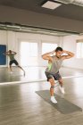 Full length of concentrated young athletic guy in sportswear doing Side Lunges exercise with elastic band while training alone in spacious fitness studio with mirror — Stock Photo