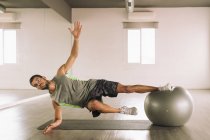 Comprimento total de forte desportista muscular fazendo Side Star Plank em forma de bola durante o treinamento em estúdio — Fotografia de Stock