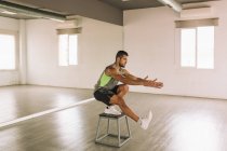 Seitenansicht eines ernstzunehmenden jungen, fitten athletischen Mannes in aktiver Kleidung, der während des Trainings im Studio eine Kniebeuge auf der Trittplattform macht — Stockfoto