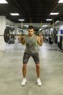 Повне тіло сильного молодого м'язового спортсмена в активному одязі, що піднімає штанги під час інтенсивних тренувань у сучасному тренажерному залі — стокове фото