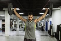 Full body of strong young muscular male athlete in activewear lifting barbells during intense workout in modern gym — Stock Photo