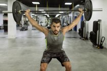 Corpo pieno di forte giovane atleta maschio muscolare in activewear sollevamento bilancieri durante l'allenamento intenso in palestra moderna — Foto stock